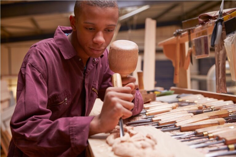 apprentice using chisel to carve wood in workshop