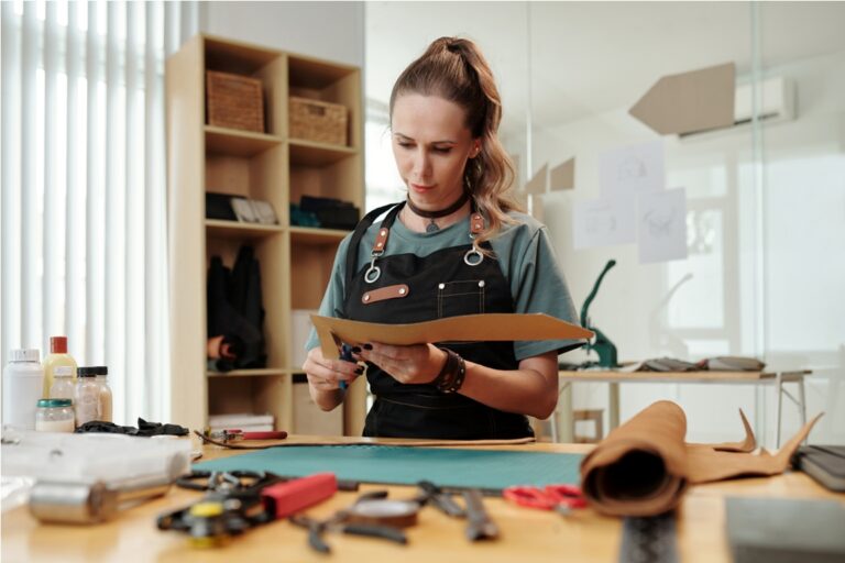 leather crafter cutting out cardboard sewing pattern of new bag